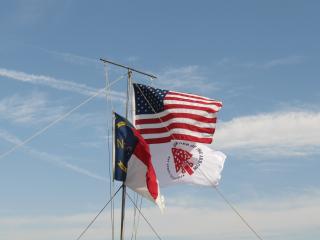 On the riverside, North Carolina, United States of America and Order of the Arrow flags fly.